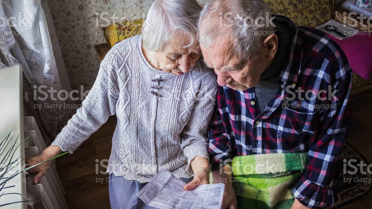 Bild - Den äldre kvinnan och mannen håller gasräkningen framför värmeelementet. Betalning för uppvärmning på vintern.